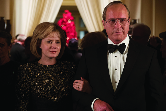 A man in a black tuxedo and bowtie stands next to a woman in a black lace dress.