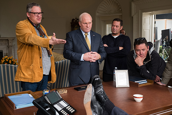 Four men stand and sit around a wooden table in an indoor setting.