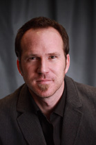 A man with short brown hair and a goatee wearing a dark blazer and shirt.