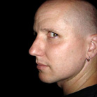 A profile view of a bald man looking toward the left against a black background.