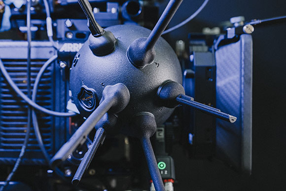 A black spherical device with several long, thin rods extending from its surface, connected to dark electronic gear.