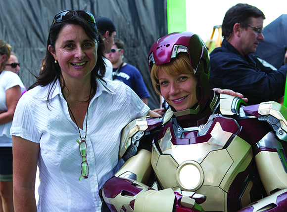 A woman in a white shirt smiles next to a person wearing a detailed Iron Man suit.