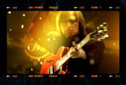 A person with long hair and sunglasses playing a red electric guitar under bright, warm stage lights.