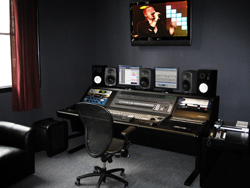 A large mixing console with multiple computer monitors and studio speakers in a dark recording studio.