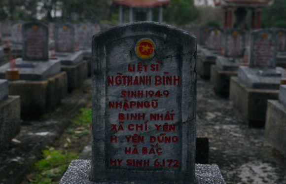 A grey stone headstone with red Vietnamese text and a yellow star emblem in a cemetery.