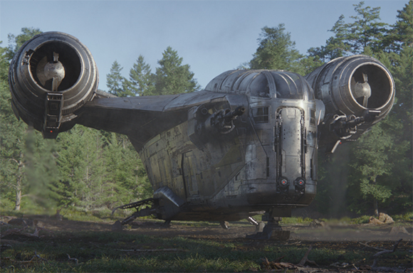 A large, metallic, weathered grey spacecraft with two massive circular engines sits in a forest clearing.