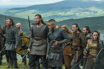 A group of warriors in textured leather and chainmail armor standing on a green hillside overlooking mountains.