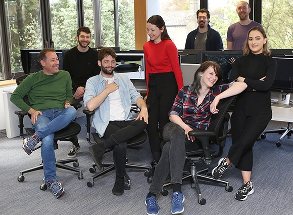 Seven diverse colleagues smiling and posing together in a bright, modern office space.