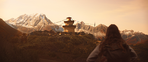 A person with a backpack looks toward a stone stupa and snow-capped mountains under a golden sky.
