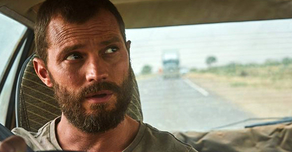 A bearded man sits in a car, looking intently out of the side window.