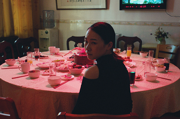 A woman in a black top sits at a large round table filled with various dishes and drinks.