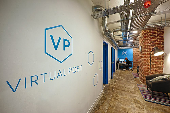 A white wall features a blue Virtual Post logo next to a hallway leading to an office space.