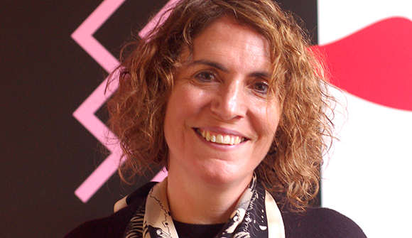 A smiling woman with curly brown hair wearing a patterned scarf.
