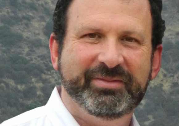 A man with dark hair and a salt-and-pepper beard wearing a white shirt.