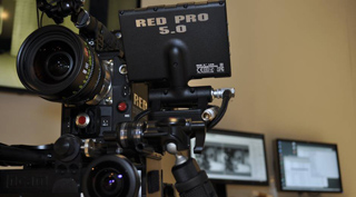 Close-up of a professional RED cinema camera with a mounted RED PRO 5.0 monitor and large lens.