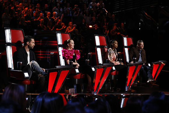 Four judges sit in large, red, stylized chairs on a dark television studio stage.