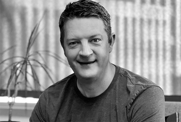Black and white portrait of a man with short hair smiling at the camera.