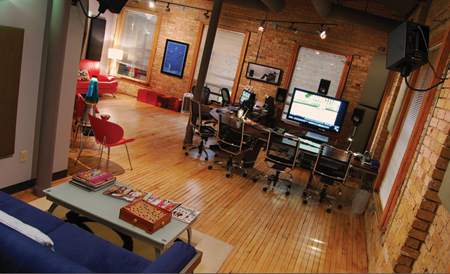 A wide view of a professional studio featuring computer workstations, brick walls, and a blue sofa.