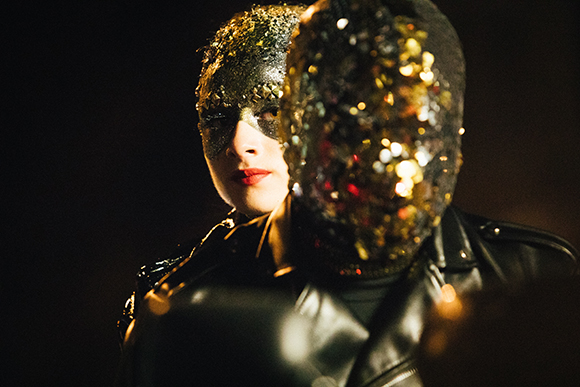 Two people in black leather outfits wearing sparkling, gold and silver textured masks.