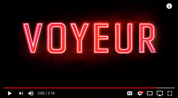 Red neon text reading VOYEUR against a dark, textured background.