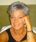 A smiling woman with short grey hair rests her chin on her hand while wearing a black tank top.