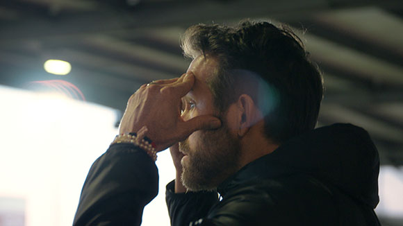 A man in profile with his hand pressed against his forehead in a dimly lit setting.