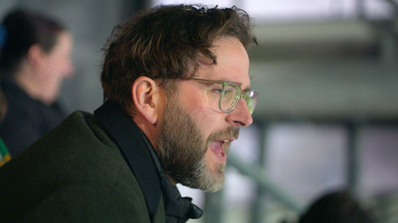 A man with brown hair, glasses, and a beard looking to the right in a profile view.