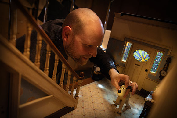 A man leans over a dollhouse to place a small dog figurine on the floor.