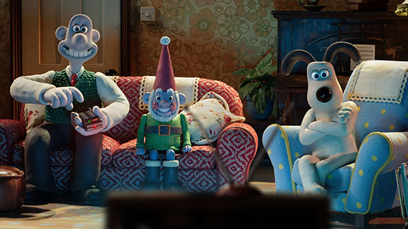 Three claymation characters sit on a sofa and armchair, looking toward a television screen.