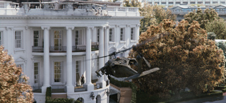 A dark military helicopter flies low past the white columns of the White House near large autumn trees.