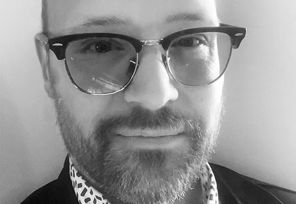 Black and white close-up portrait of a man wearing glasses and a patterned shirt.