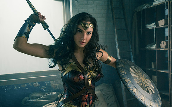 A woman in golden and red armor holds a sword aloft and a circular shield to her side.