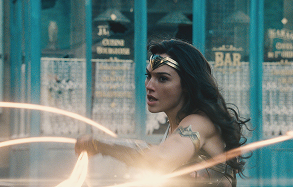 A woman with long dark hair and a gold tiara swings a glowing golden lasso in a combat stance.