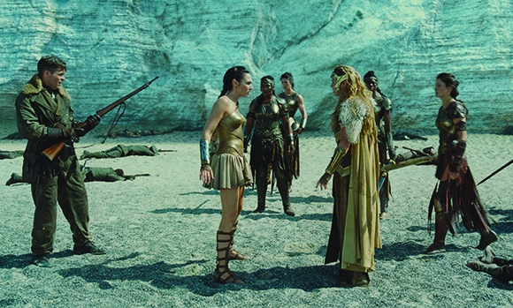A soldier in a green uniform faces a group of women dressed in ancient bronze and leather armor.
