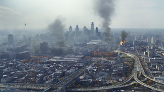 Aerial view of a city skyline with several large plumes of dark smoke rising over the buildings.