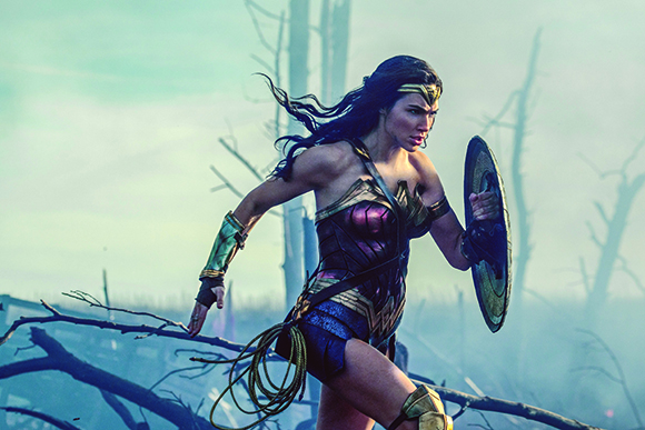A woman in Amazonian battle armor runs through a misty, desolate landscape holding a shield.