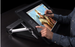 A person uses a stylus to draw a character on a large digital graphics tablet.