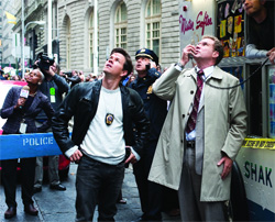 Three men in a city street look upward toward something out of frame.