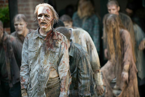 A group of people dressed as zombies with pale, decaying skin and blood-stained, torn clothing.