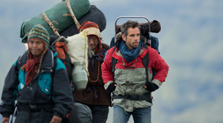 Three people trekking through a mountainous area while carrying large packs and supplies.