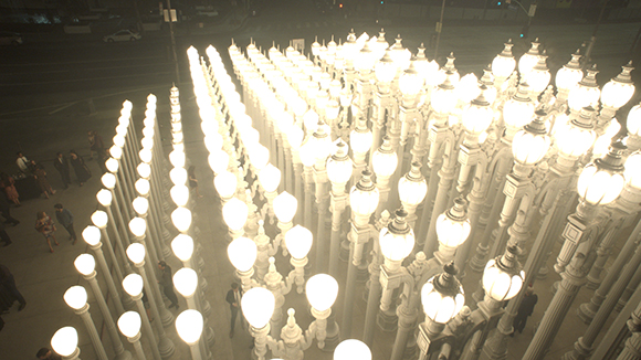Rows of tall, glowing white spherical street lamps arranged in a grid on a city sidewalk at night.