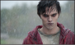 A pale man with dark, wet hair and dark circles under his eyes stands in the rain wearing a red hoodie.