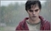 A young man with dark hair and pale skin wearing a red jacket looks toward the camera.