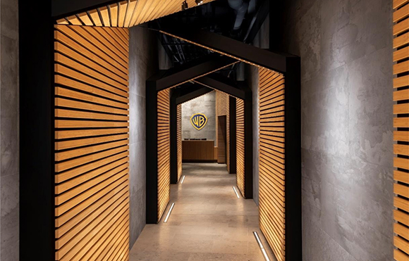 A hallway with wooden slat walls and ceiling leading to a Warner Bros. logo on a far wall.
