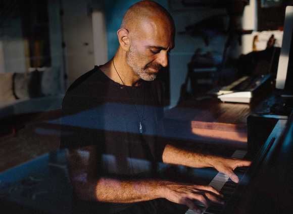 A bald man with a beard playing a piano in a dimly lit room.