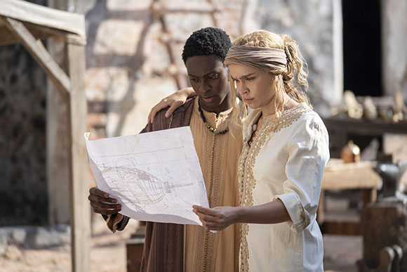 A man and a woman stand together looking at a large piece of paper with sketches on it.