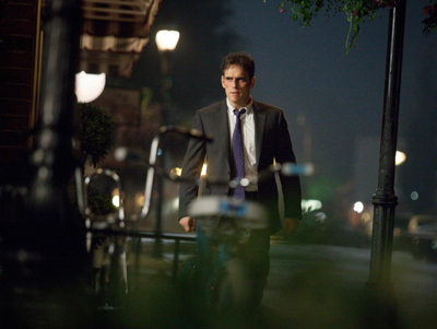 A man in a grey suit and purple tie walks down a street at night near parked bicycles.