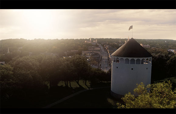 A white circular tower with a dark conical roof overlooks a town nestled among trees under a bright sunset.
