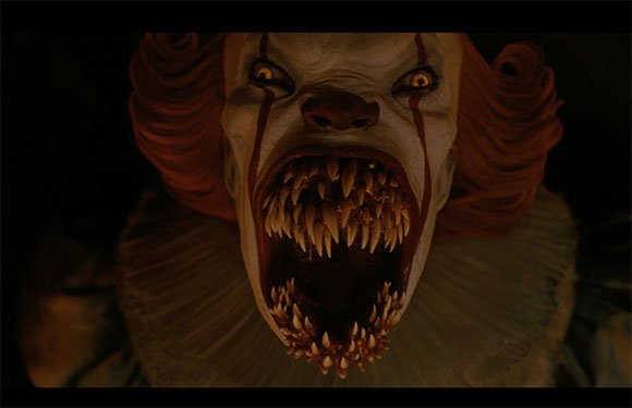 Close-up of a clown with orange hair and a mouth full of long, sharp, yellowed teeth.