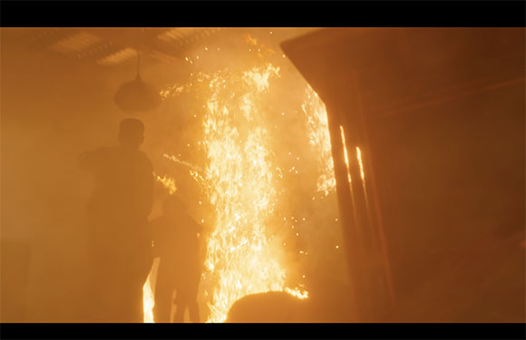 Silhouetted figures stand before a massive, bright orange explosion of fire and sparks in a dark setting.